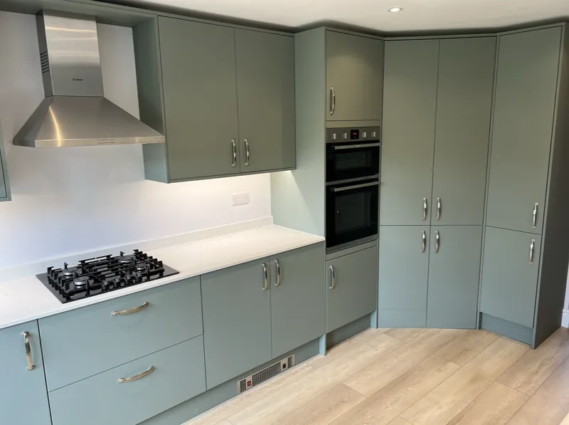 Sage green shaker kitchen with built-in double oven, gas hob, chimney extractor and wood-effect floor